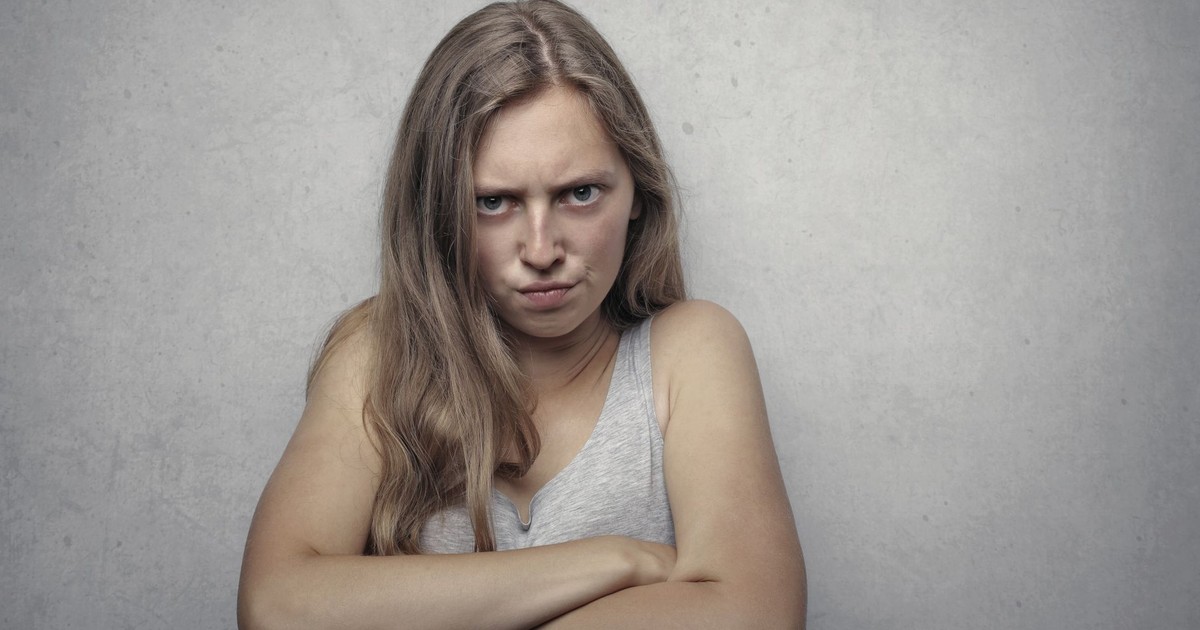 A woman with arms crossed showing a fierce expression against a gray background.