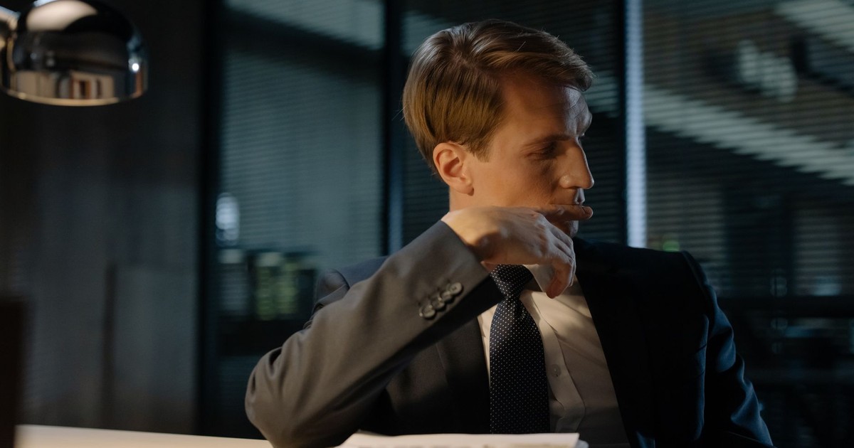 A man in a suit thoughtfully sitting at a desk in an office at night.