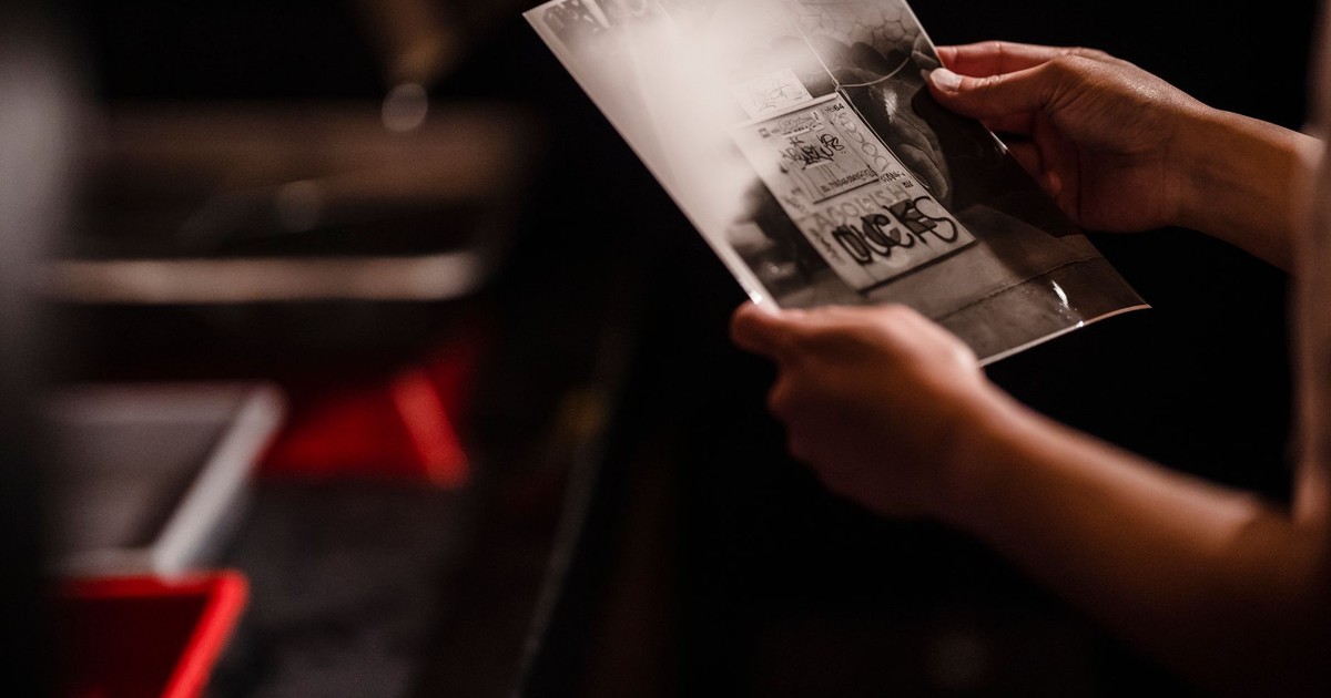 A person examines a black-and-white photograph in a darkroom setting.
