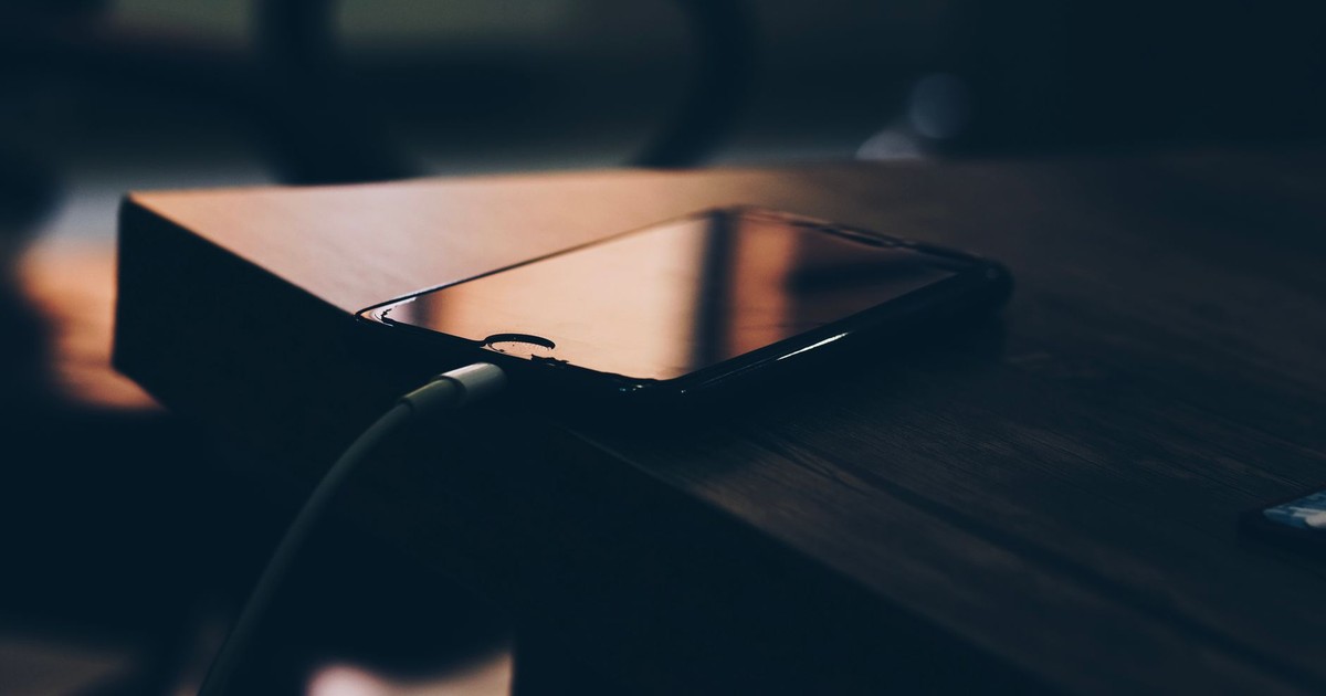 A smartphone connected to a charger lying on a wooden table indoors.