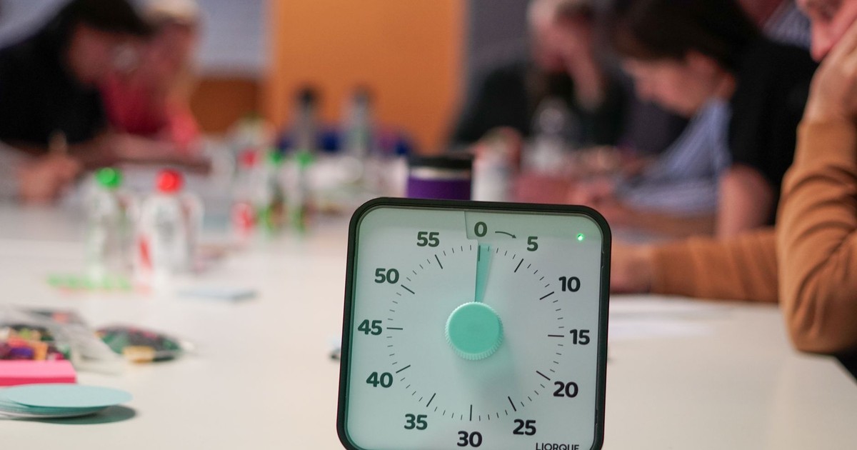 Timer on a table with blurred people in an office meeting setting, emphasizing focus.