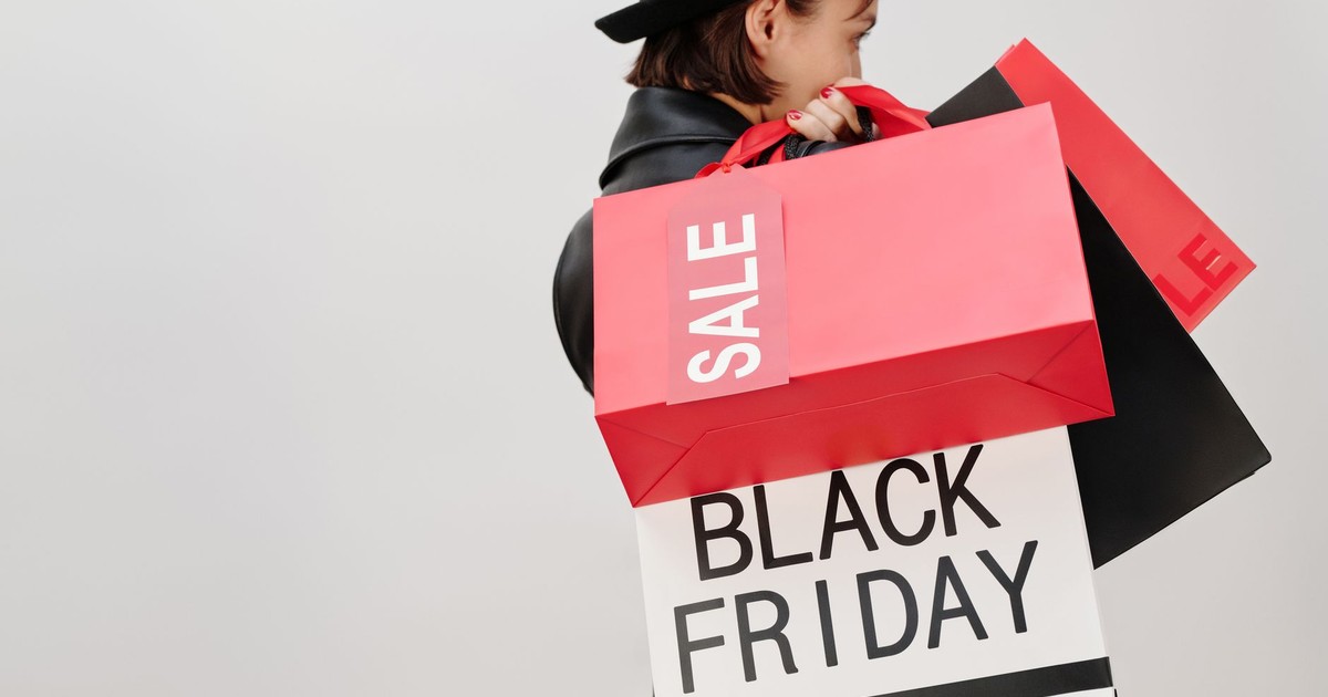A stylish woman carrying Black Friday sale shopping bags against a neutral background.