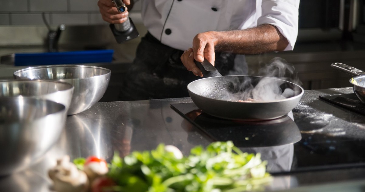 Chef prepares food in a sleek kitchen using a frying pan on an induction cooktop.