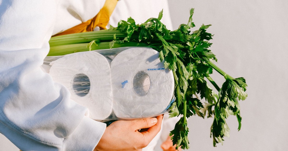 Close-up of hands holding toilet paper and celery stalks, emphasizing daily essentials.