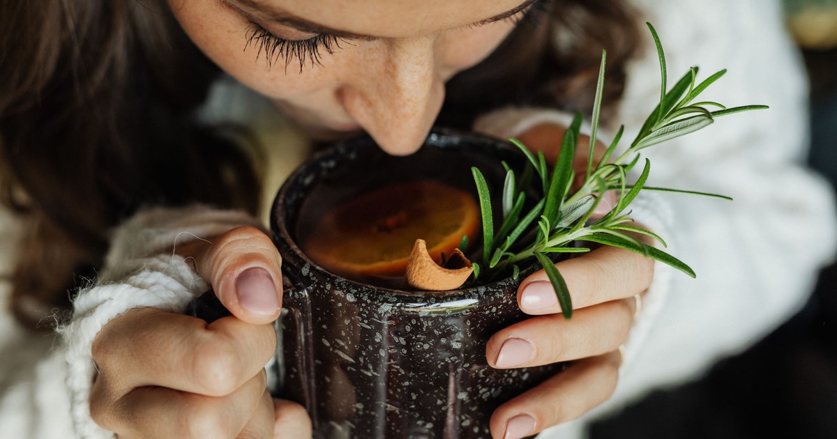 Woman savoring hot herbal tea with rosemary and orange, close-up view.