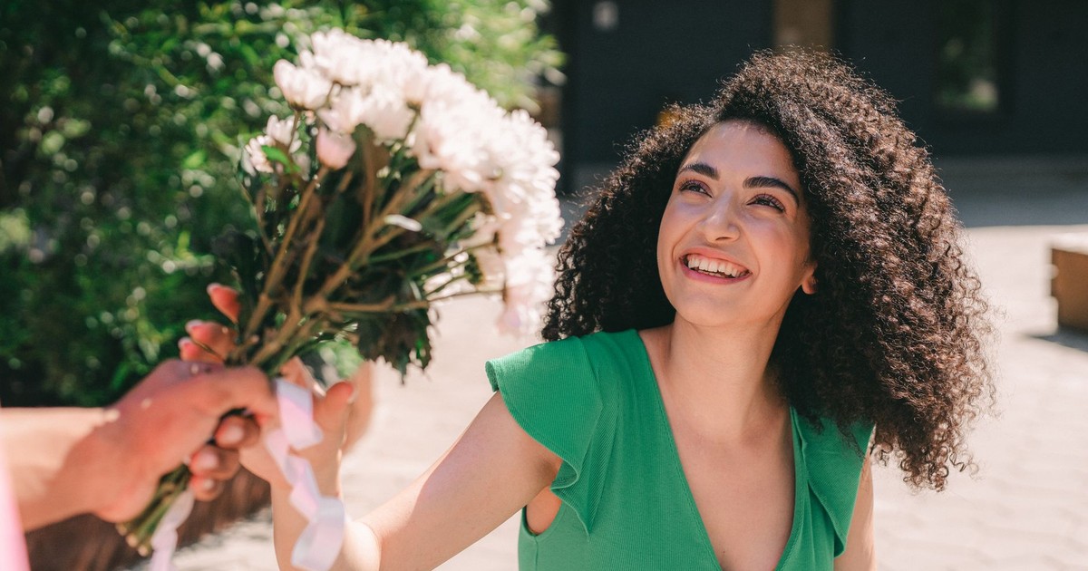 A woman smiles brightly while receiving a bouquet in an outdoor urban setting.