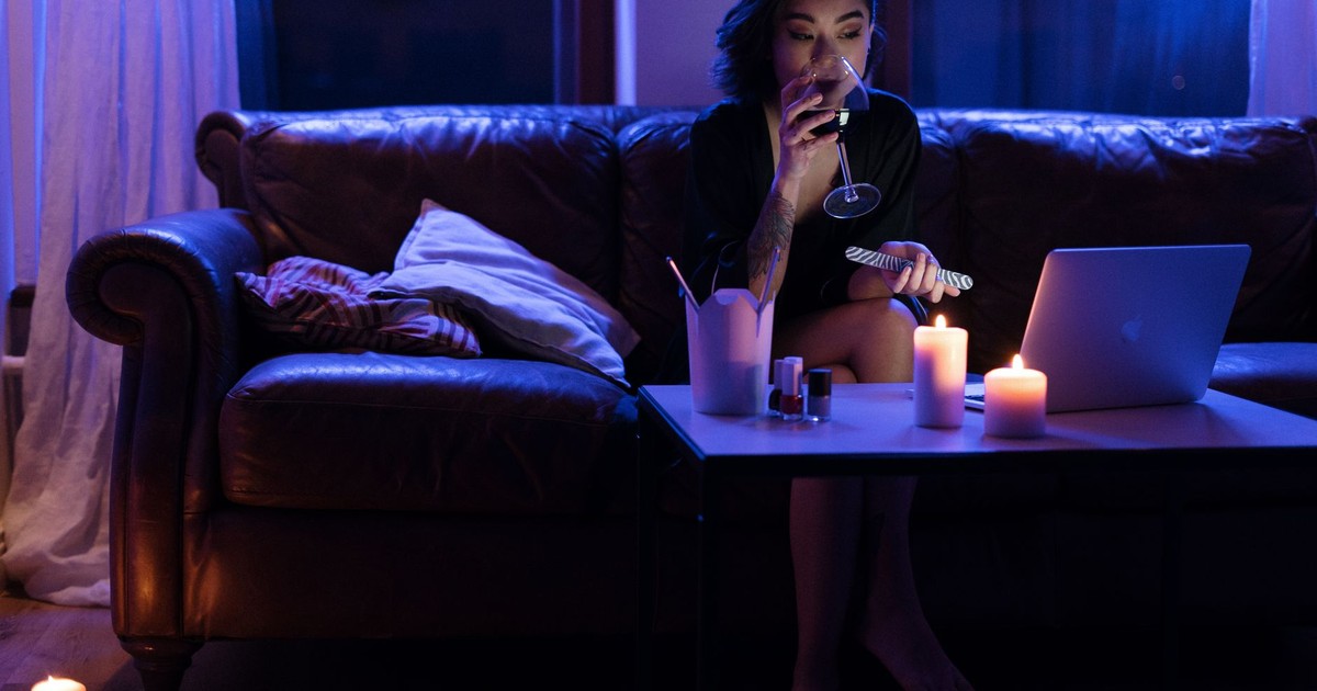 Woman relaxing with wine and laptop on a cozy evening illuminated by candles.