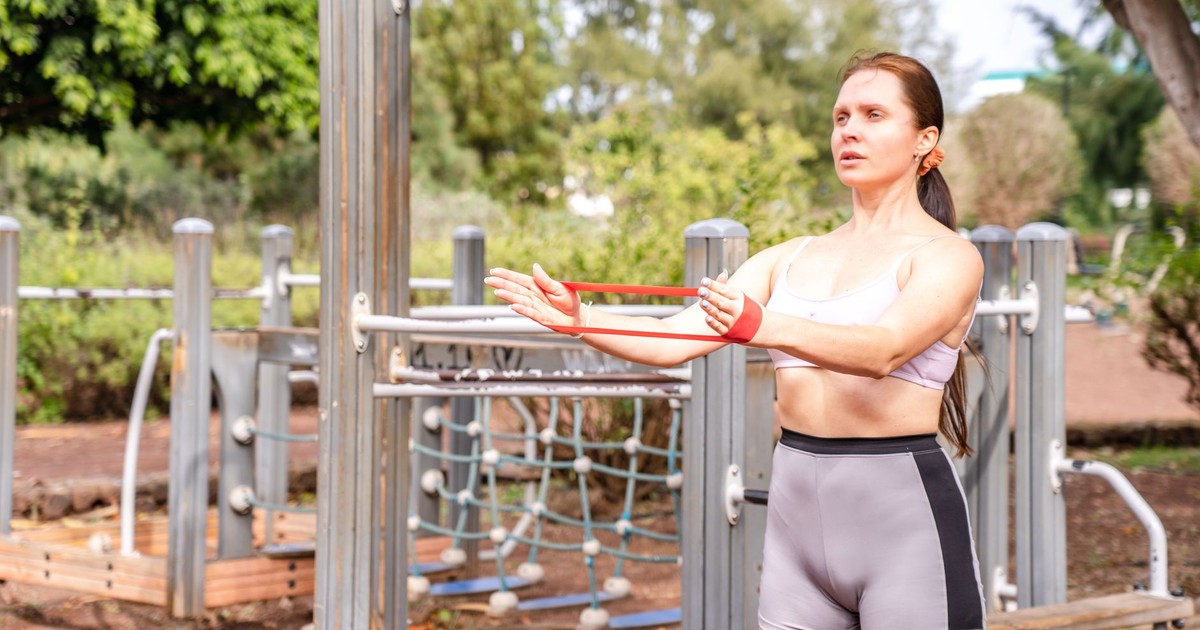 Woman doing resistance band workout in an outdoor park setting.