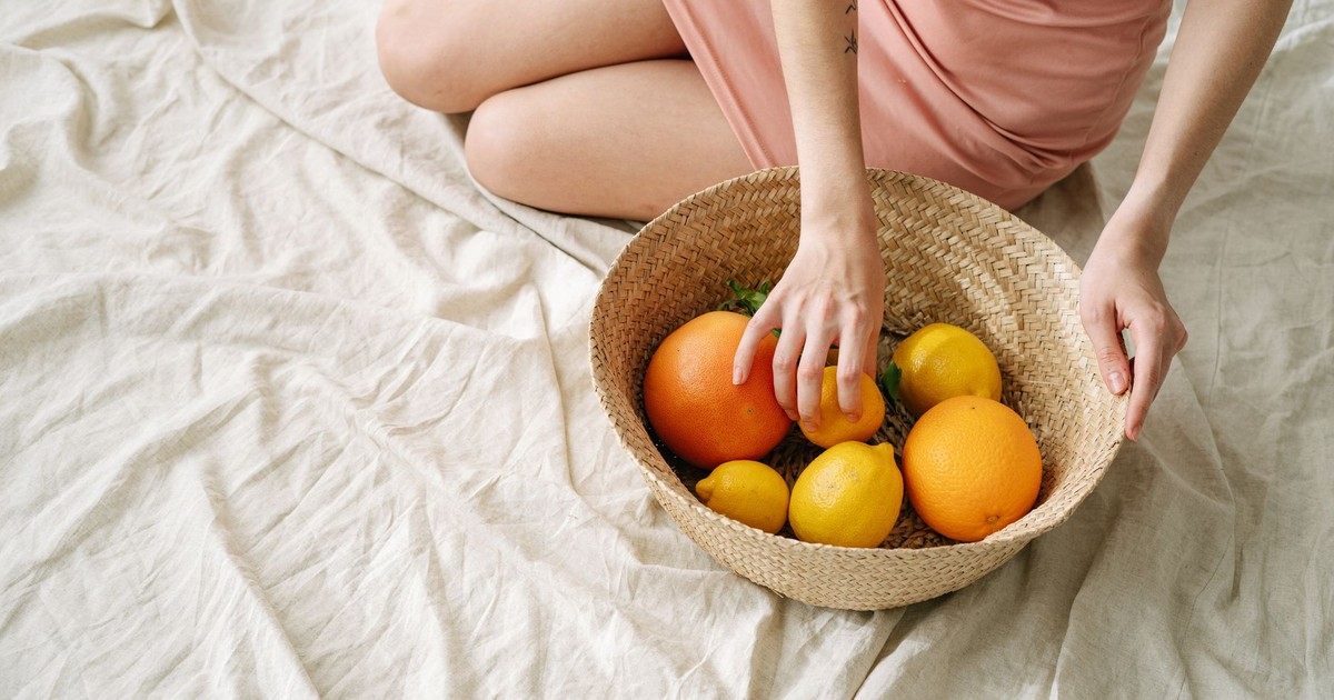 A woman in a pink dress holding a basket of fresh citrus fruits, including oranges and lemons.