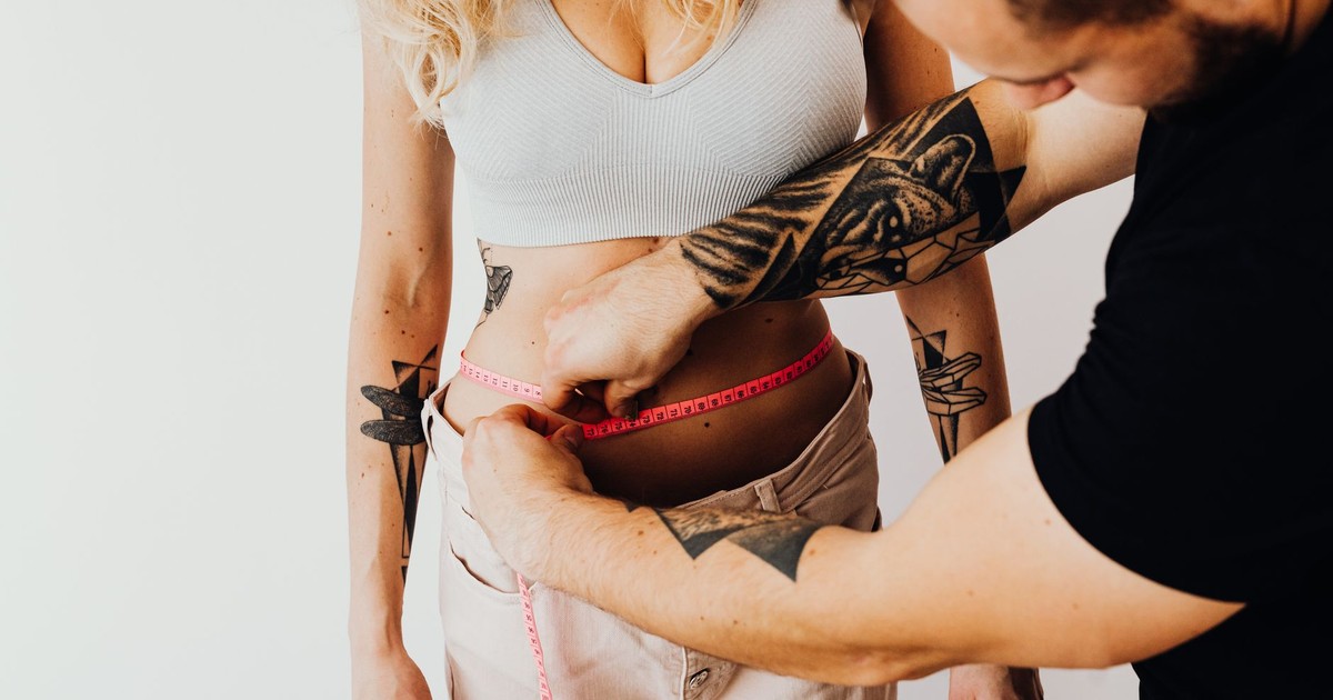 A man measures a woman's waist with a tape measure, focusing on fitness and health goals.