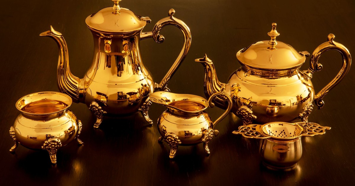 A luxurious golden teapot set with intricate designs beautifully arranged on a dark surface.