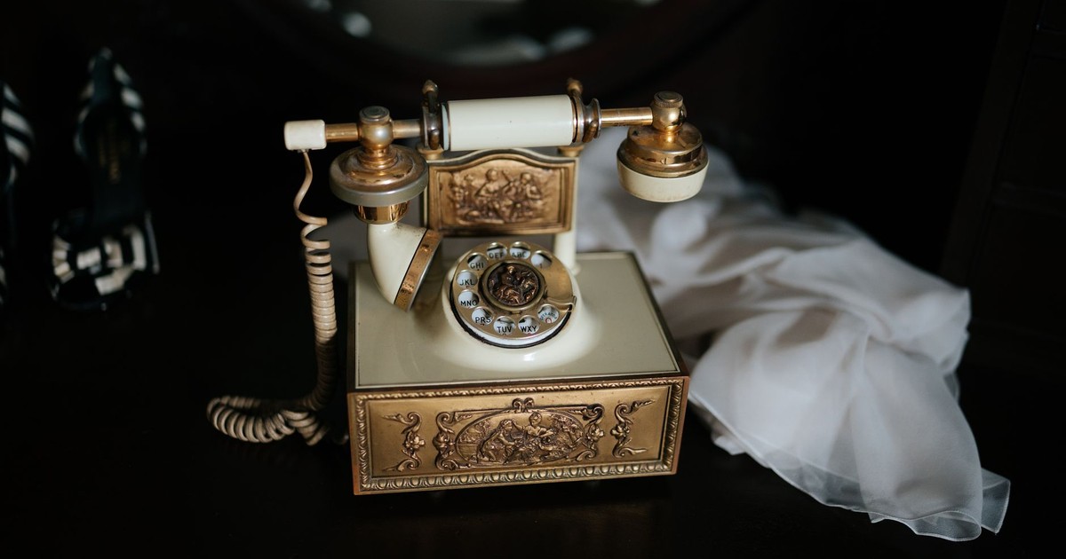 Antique rotary telephone with ornate gold details, displayed indoors with a classic decorative style.