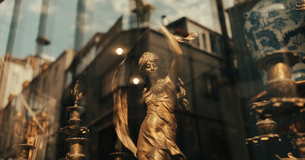 A brass statue elegantly displayed behind a glass window, reflecting outdoor architecture.
