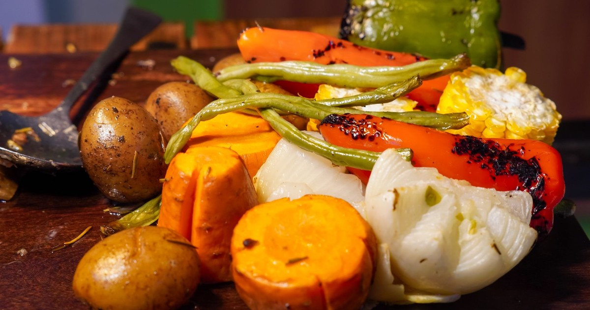 A vibrant assortment of grilled vegetables including bell peppers, beans, and potatoes on a wooden board.