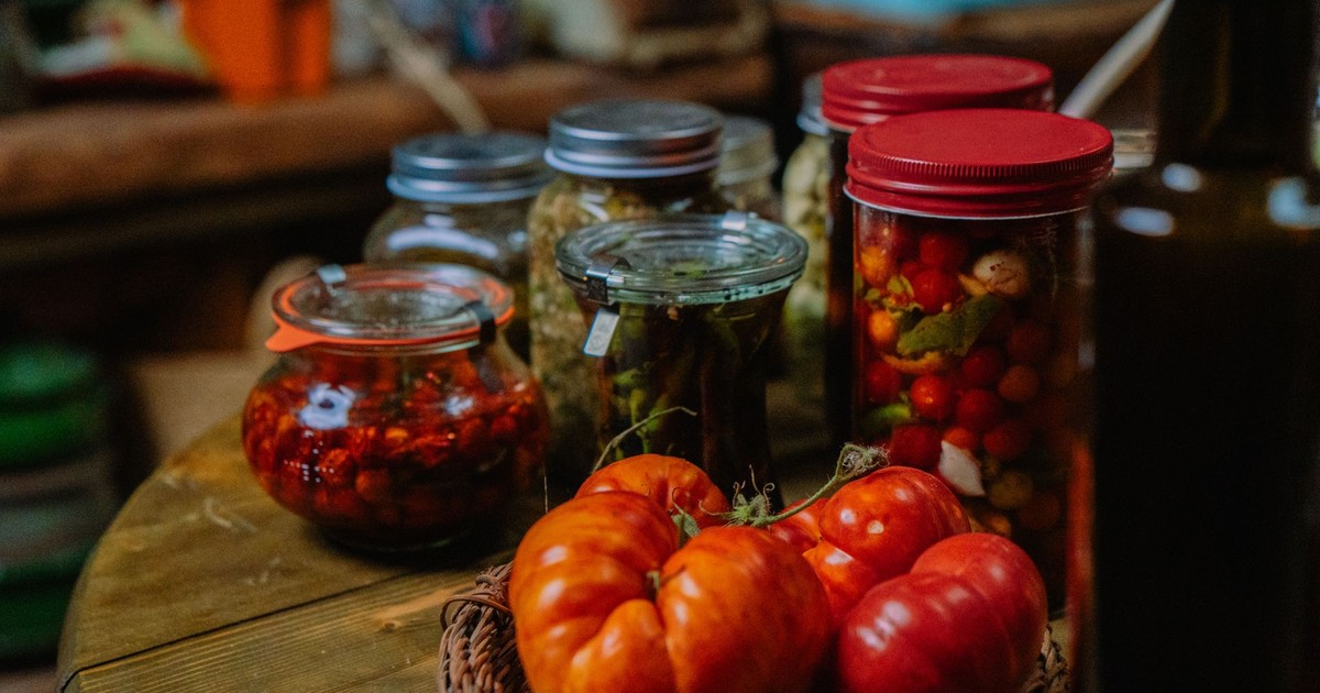 A rustic kitchen setup featuring fresh tomatoes and various pickled vegetables in glass jars.