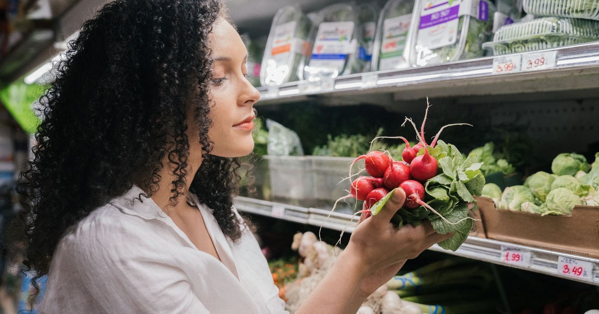 Woman in grocery store choosing fresh radishes from the vegetable aisle.