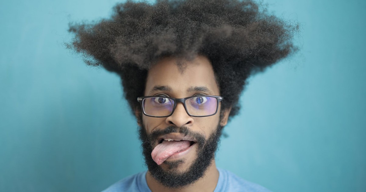 A playful portrait of a man with afro hair and glasses making a fun facial expression.