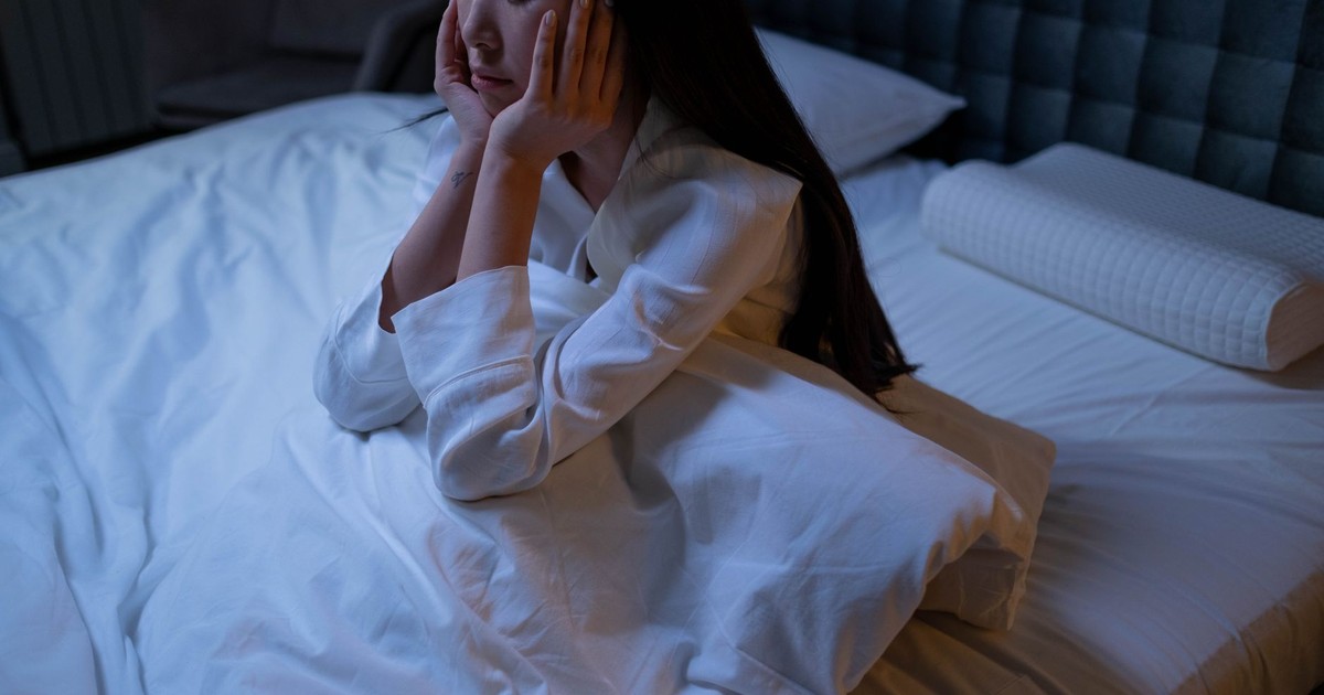 An Asian woman in bed at night, experiencing insomnia and loneliness, deep in thought.