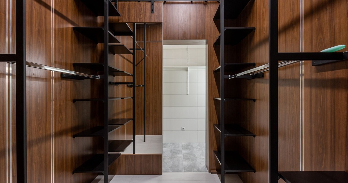 Empty black shelves and racks placed in modern walk in closet with brown walls and mirror with reflection at home