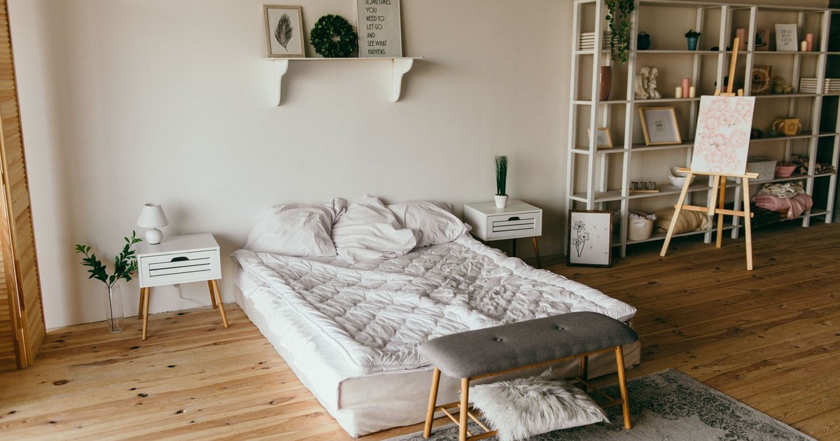 Spacious modern bedroom with minimalist decor, featuring a low bed, wooden floors, and shelf storage.