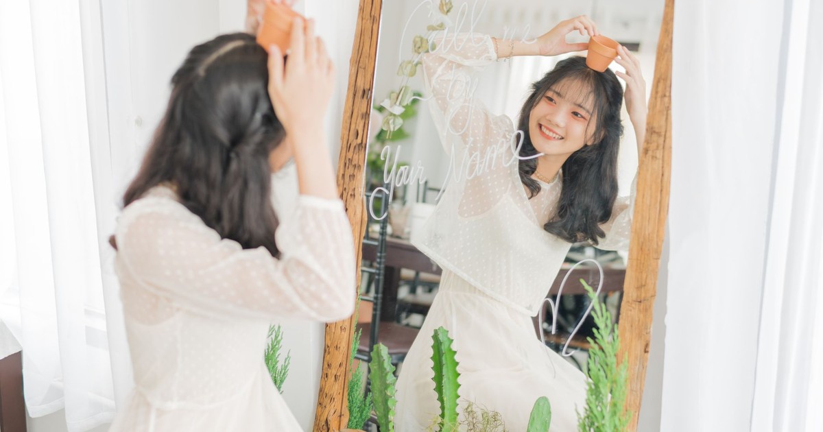 Smiling woman holding a small pot in front of mirror with plants, embracing nature indoors.