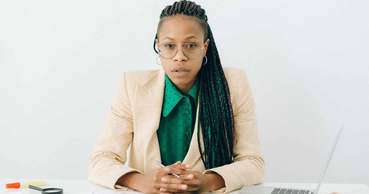 Black woman in business attire at a desk with laptop and charts, looking focused.