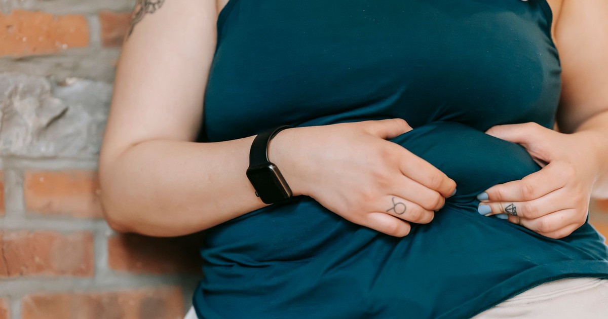 Crop anonymous plus size female demonstrating and touching belly while leaning on brick wall