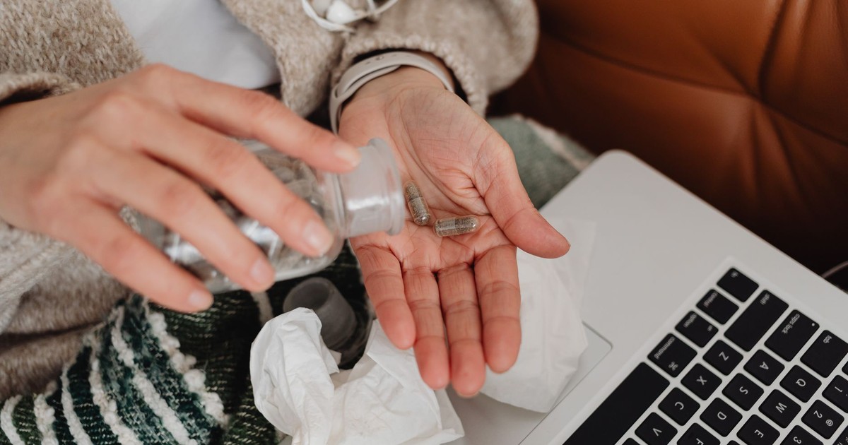 A person holding pills near a laptop, symbolizing telemedicine use.