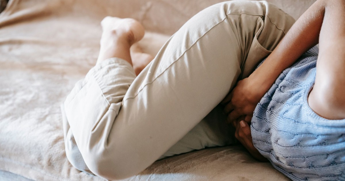 Crop anonymous barefoot female in casual outfit lying on couch while having acute stomach ache
