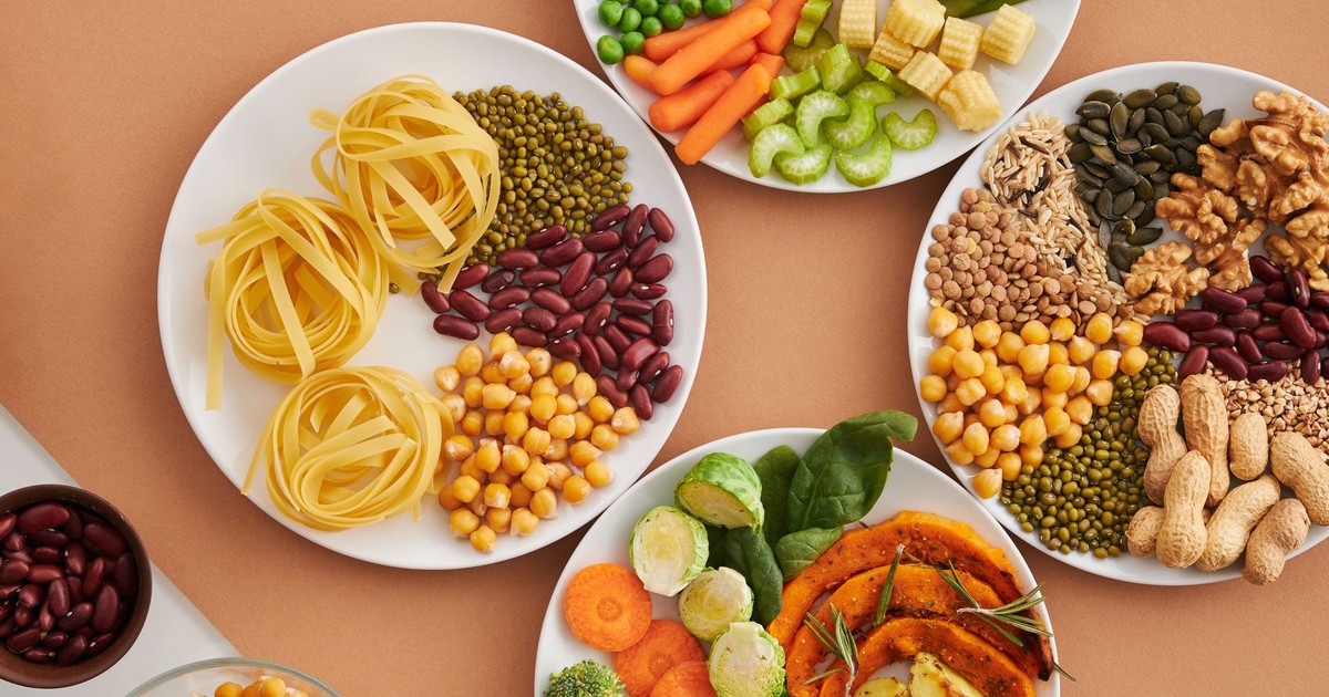 A vibrant mix of legumes, vegetables, nuts, and pasta arranged on white plates showcasing a balanced, healthy diet.