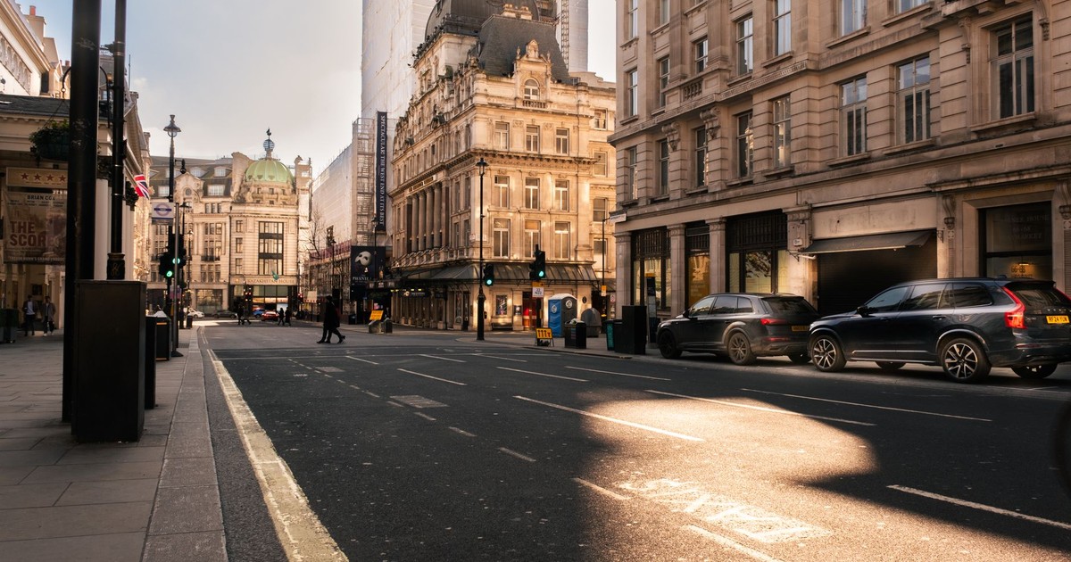 A sunlit street in London's historic district, showcasing Victorian architecture and modern vehicles.