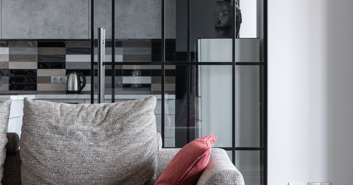 Cozy living room featuring a textured sofa with a red pillow and a modern kitchen backdrop.