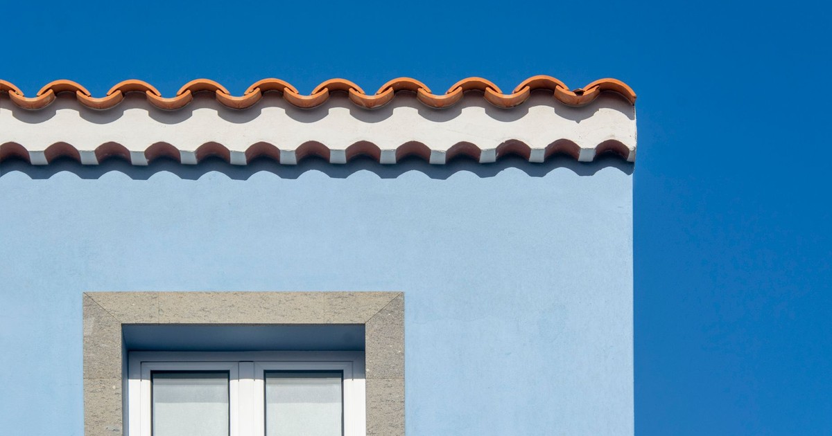 Bright blue house facade with distinctive orange roof tiles under a clear sky.