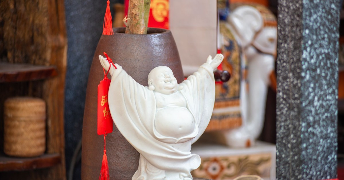 White Laughing Buddha statue with red tassel decoration in vibrant Asian interior.