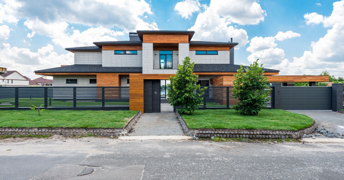 Facade of contemporary luxury villa building with lawn and green trees under blue sky with clouds