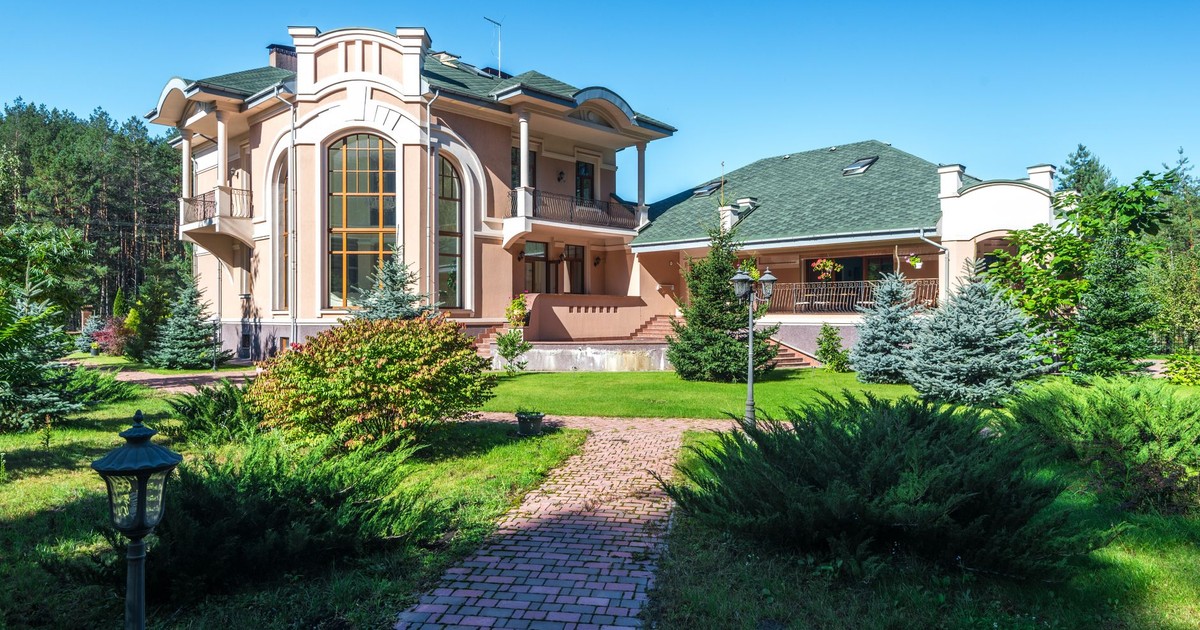 Beautiful mansion in sunny weather, surrounded by lush greenery and a clear blue sky.