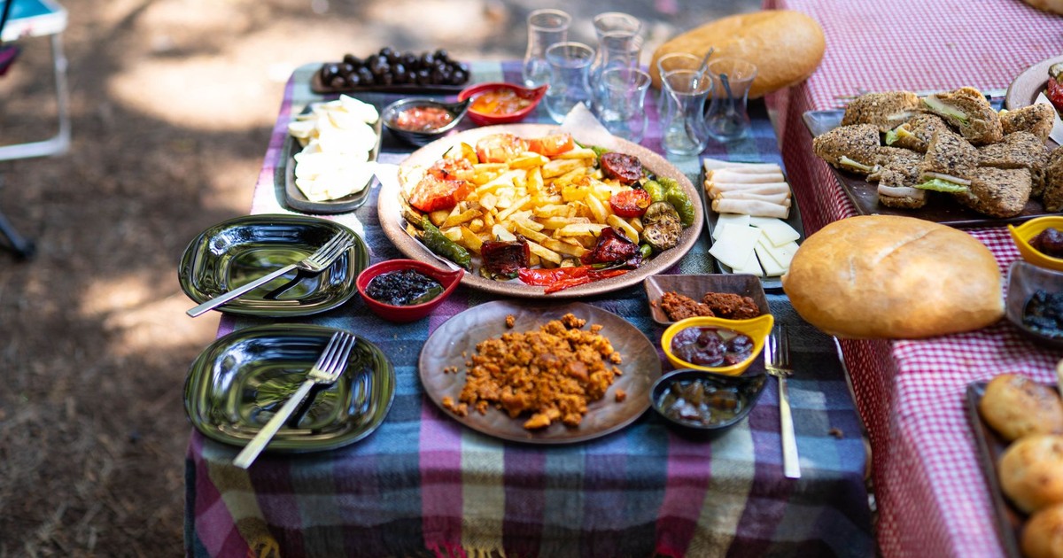 A vibrant outdoor picnic setup with various fresh dishes, bread, and tableware on a checkered cloth.