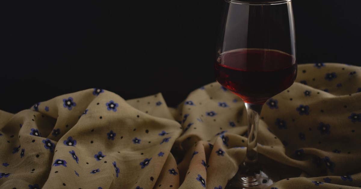 Sophisticated still life with a glass of red wine and floral fabric, set against a dark background.