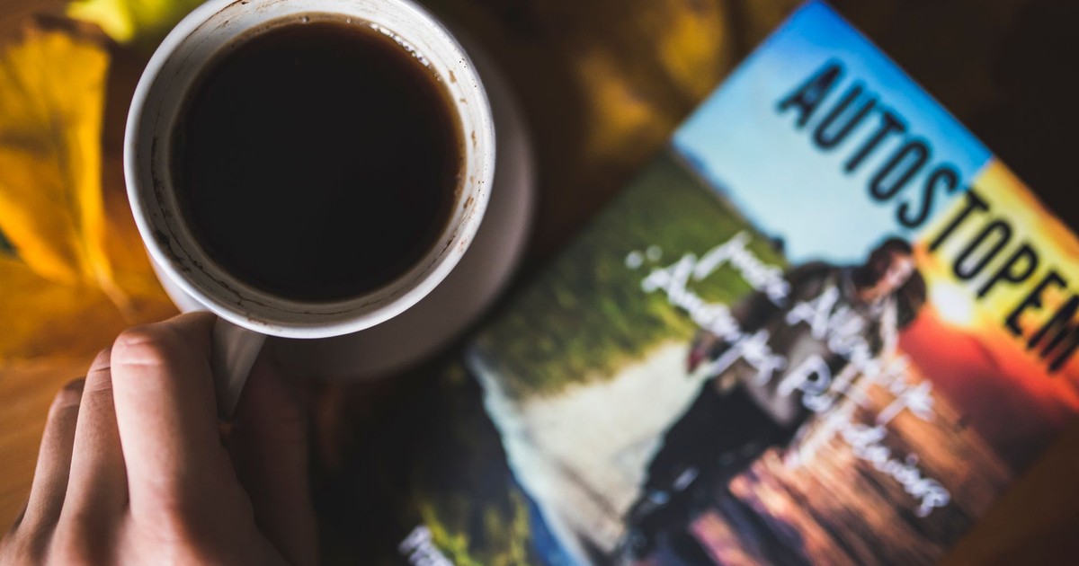 A warm cup of coffee beside a travel book on an autumn-themed surface.