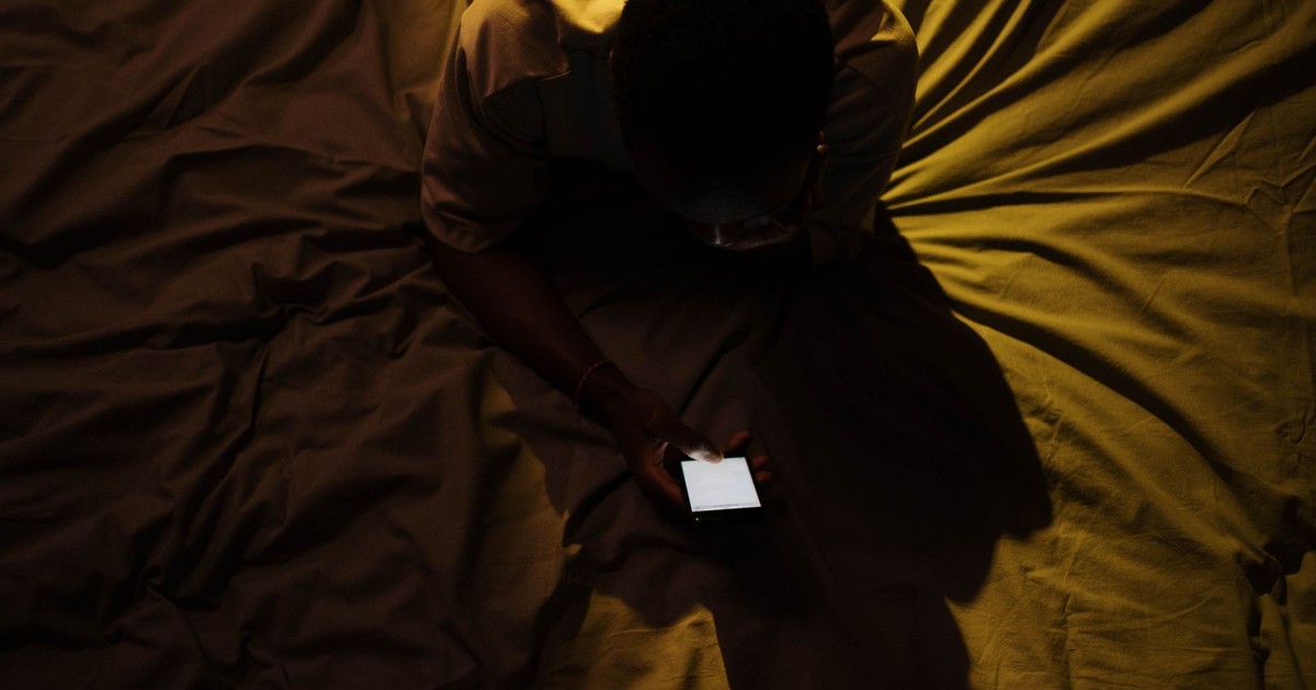 Overhead shot of a person using a smartphone on a bed, creating a moody atmosphere.
