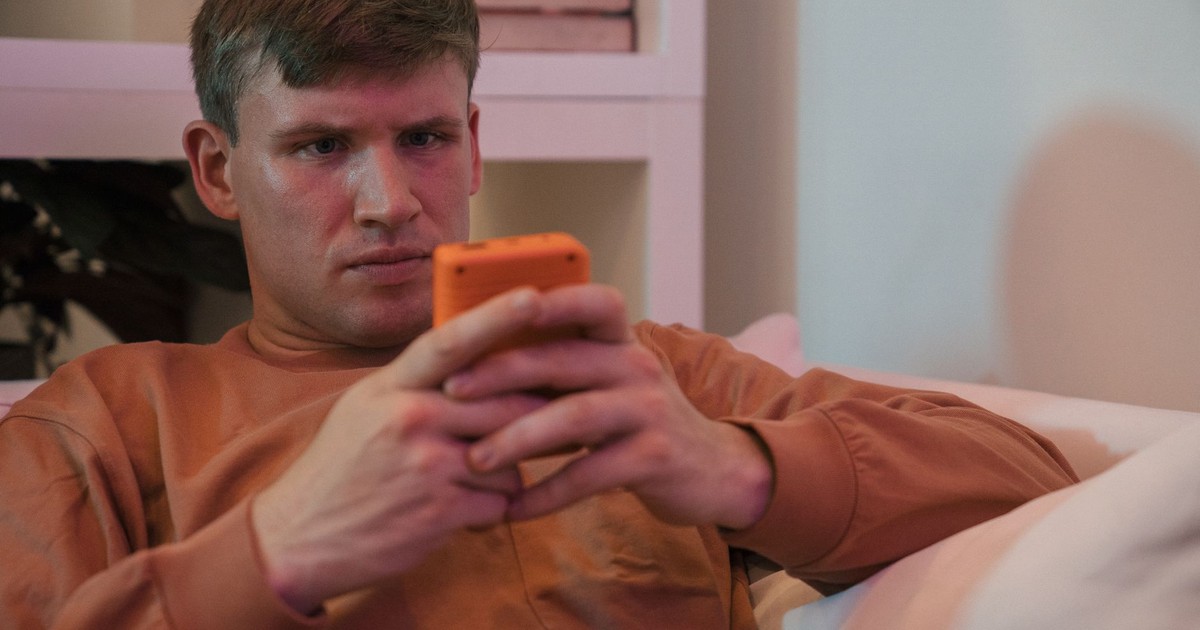 A man in casual attire intensely focused on his smartphone while relaxing indoors.