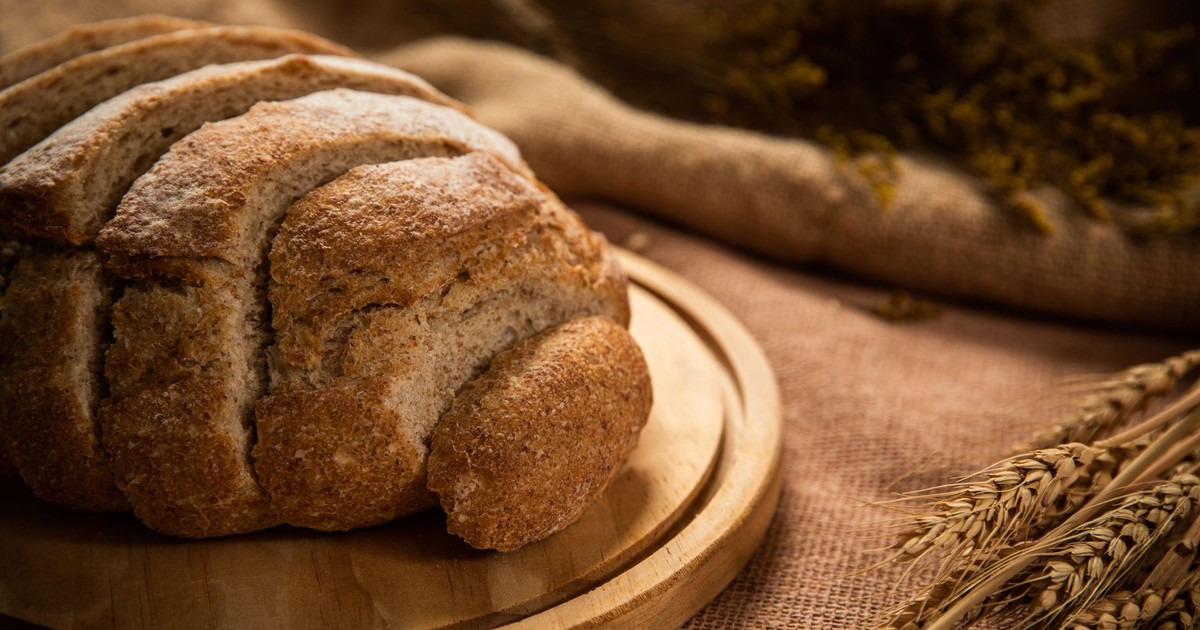 Delicious freshly baked whole wheat bread loaf on a wooden board with wheat in the background.