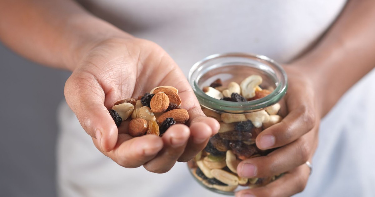 A person's hands holding a glass jar and a handful of assorted nuts, perfect for healthy snacking.