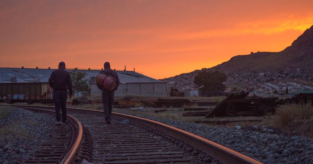 Two men walking along railway tracks during a stunning sunset in Chihuahua, Mexico.