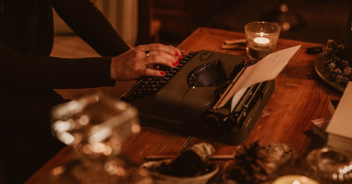 Close-up of hands typing on a vintage typewriter in a cozy, candle-lit setting.