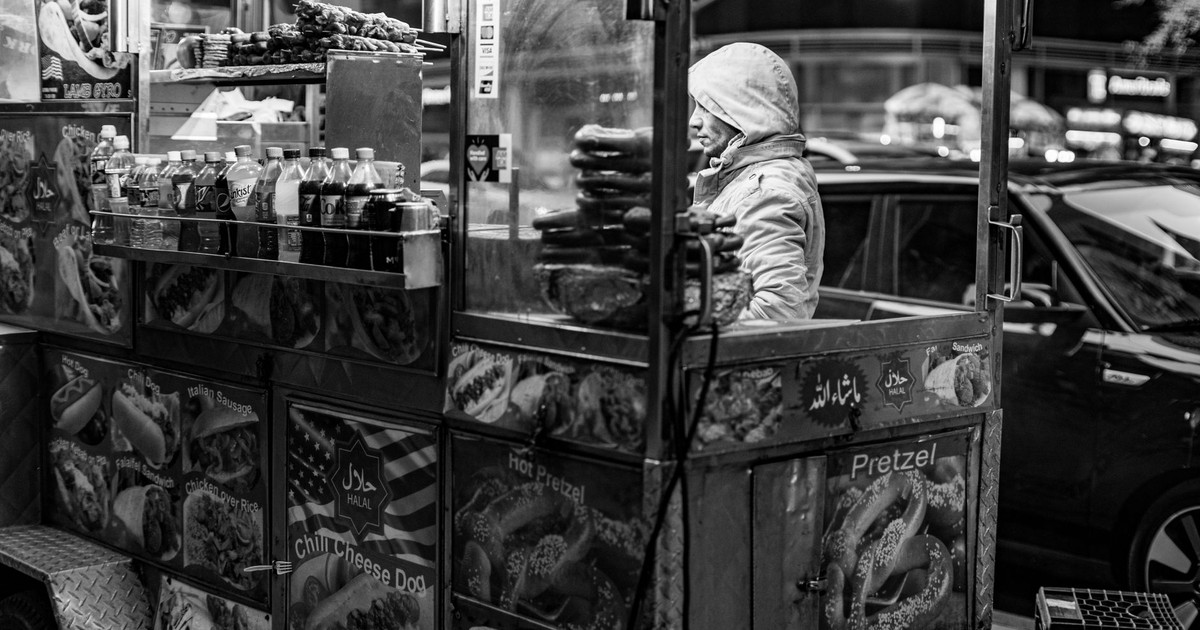 Monochrome image of a street food vendor in New York City selling hot dogs and pretzels.
