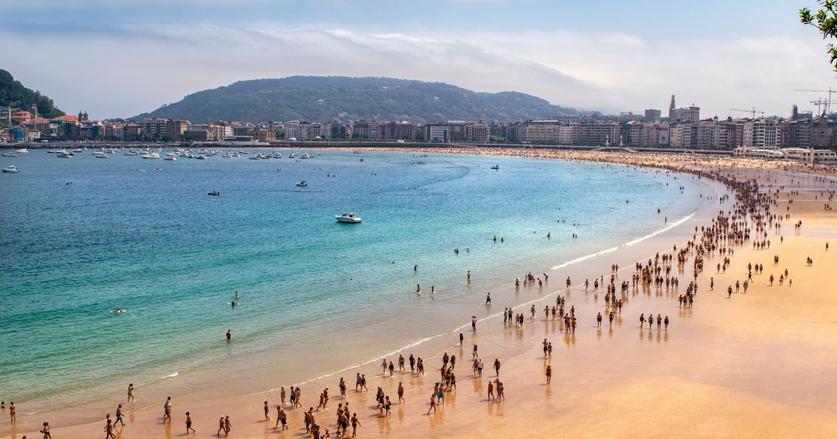 Crowds enjoy a bustling day at San Sebastián beach with clear sky and turquoise water.