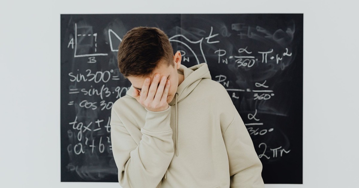 A frustrated student in a classroom standing in front of a blackboard filled with trigonometry equations.