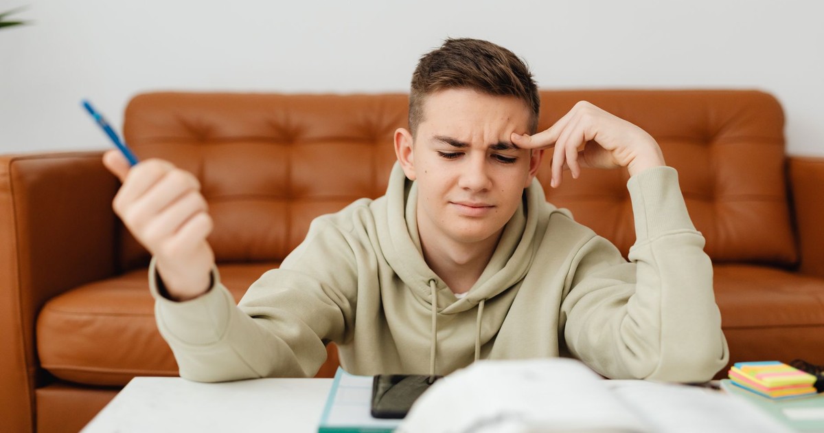 Teen boy concentrating on homework, looking stressed and thoughtful in a cozy indoor setting.