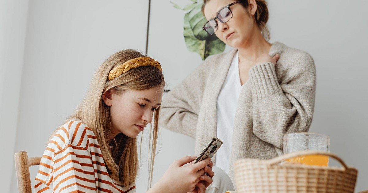 A mother discusses with her daughter engrossed in her phone during breakfast indoors.